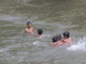 Boys swim in the river as their mother haul mud to sell to a cement factory nearby. 