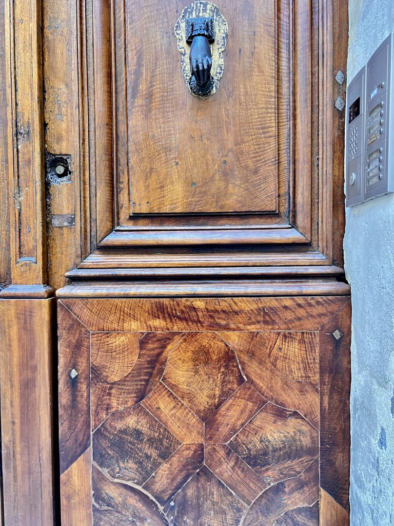 Gutsy Traveler: Discover the charm of a wooden door with a decorative hand-shaped knocker, intricate paneling, and an intercom to the right—a perfect starting point for your next adventure like a France River Cruise for Travelers 50+.