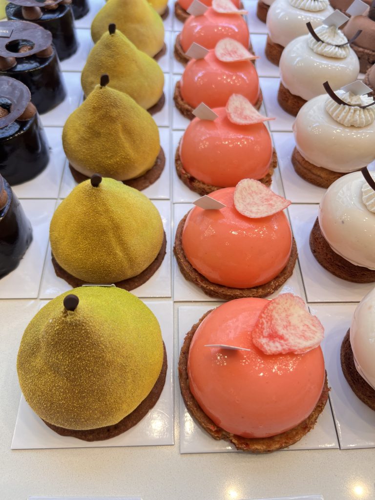 Gutsy Traveler: Experience a France river cruise for travelers 50+, where you'll savor an assortment of dome-shaped pastries, including yellow, pink with leaf decorations, and white with chocolate pieces, elegantly arranged in rows on square bases as you glide along scenic waterways.