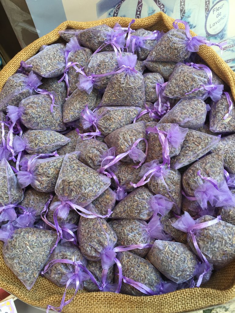 Gutsy Traveler: A pile of small mesh bags filled with dried lavender, each tied with a purple ribbon, evokes the serene charm of a France River Cruise for travelers 50+, nestled elegantly in a woven basket.