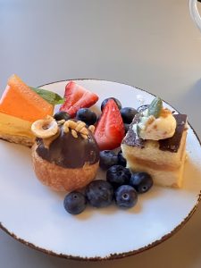 Gutsy Traveler: A white plate with assorted desserts, including a chocolate pastry, a slice of layered cake, a cheesecake slice, and fresh strawberries and blueberries—perfect for your Quebec City weekend guide of things to do and taste.