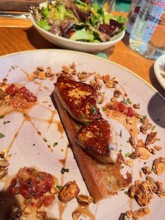 Gutsy Traveler: A plated dish with seared foie gras on toast, garnished with nuts and sauce, alongside a mixed green salad and a glass of water—a must-try for any Quebec City weekend guide.
